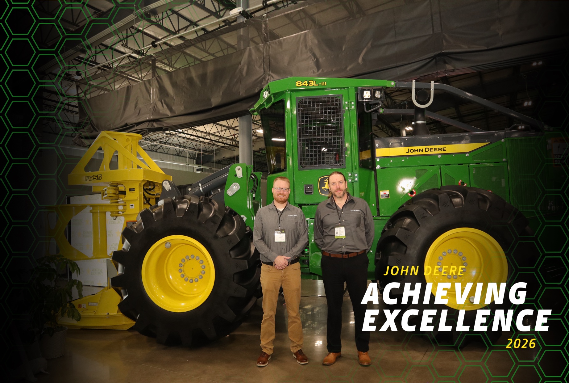 Lee Gulbrandson and Tyle Chrstensen pose in front of John Deere peice of logging equipment while at an Acheiving Excellence reception.